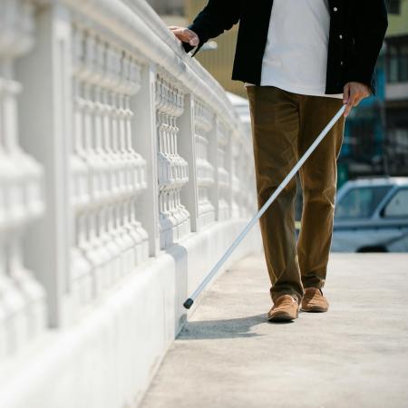 A man walks across a bridge with a mobility cane.
